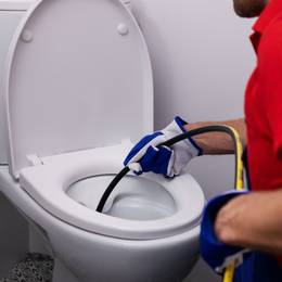 A man cleaning a toilet with a hose.