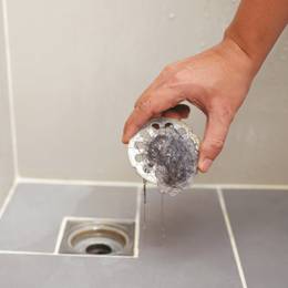 A person cleaning a shower drain with a brush.