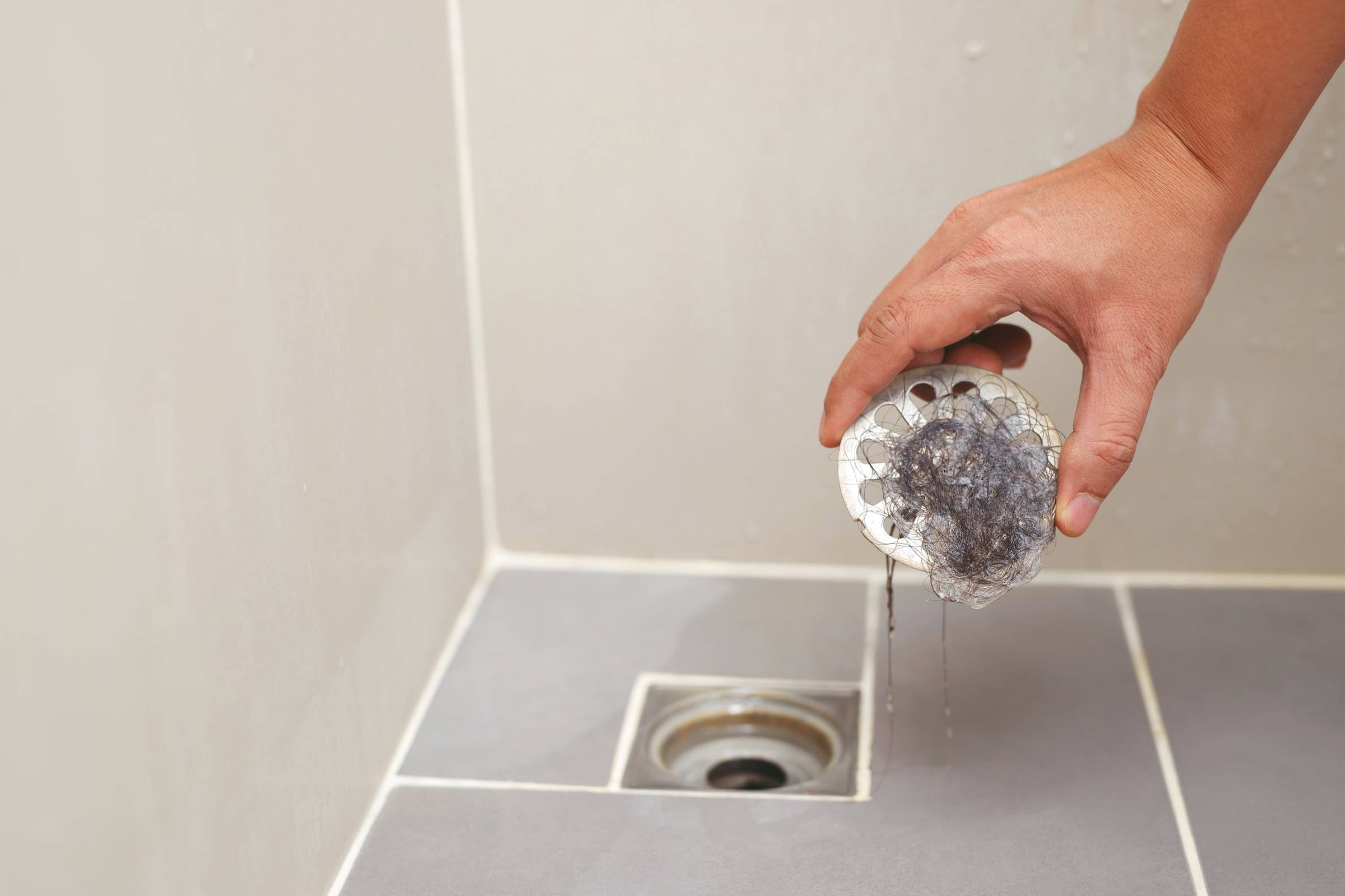 A person cleaning a shower drain with a brush.